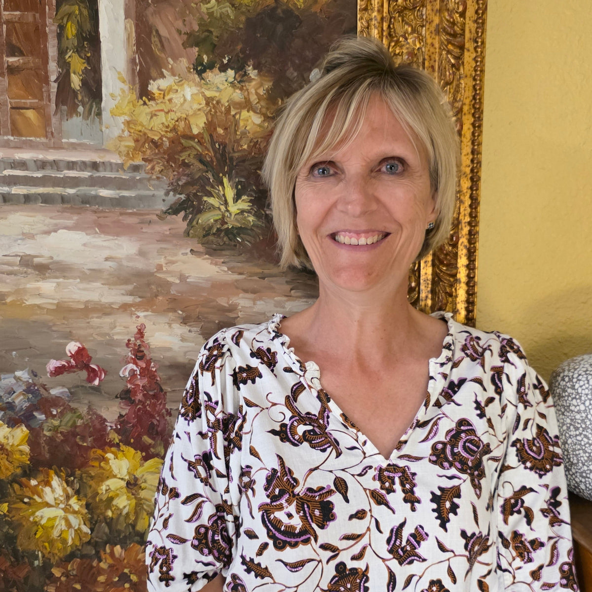 picture of woman with short blond hair in front of painting