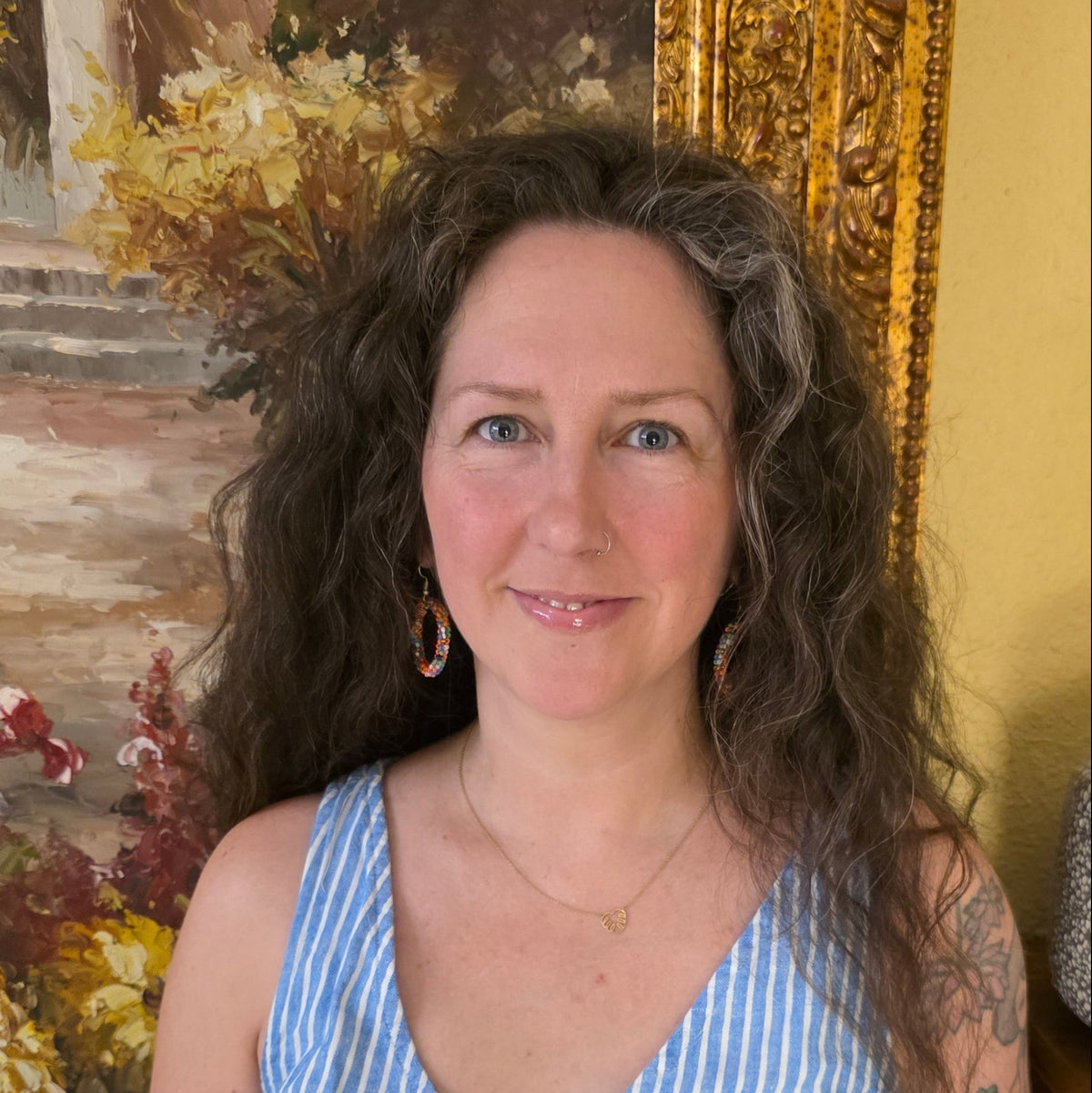 picture of woman with long curly brown hair in front of painting