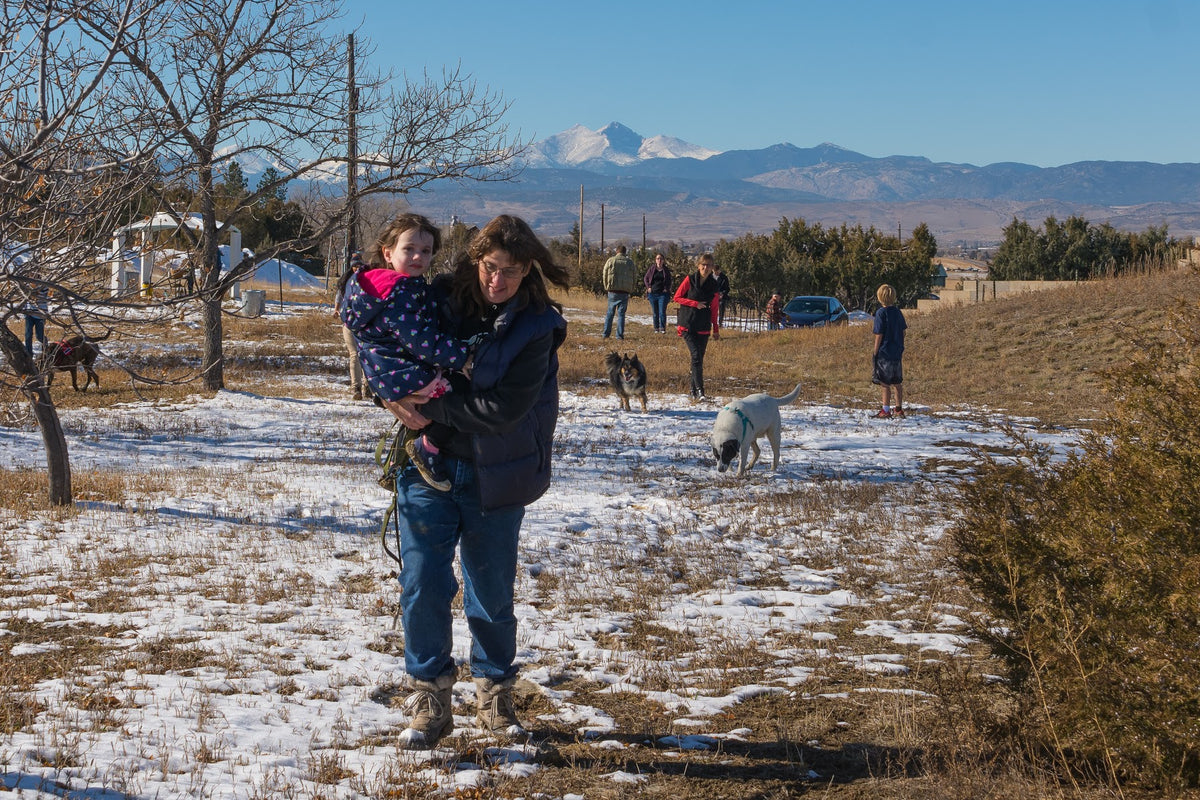 woman carrying child with other adult, children and dogs in the background aon the Resiliency Project land