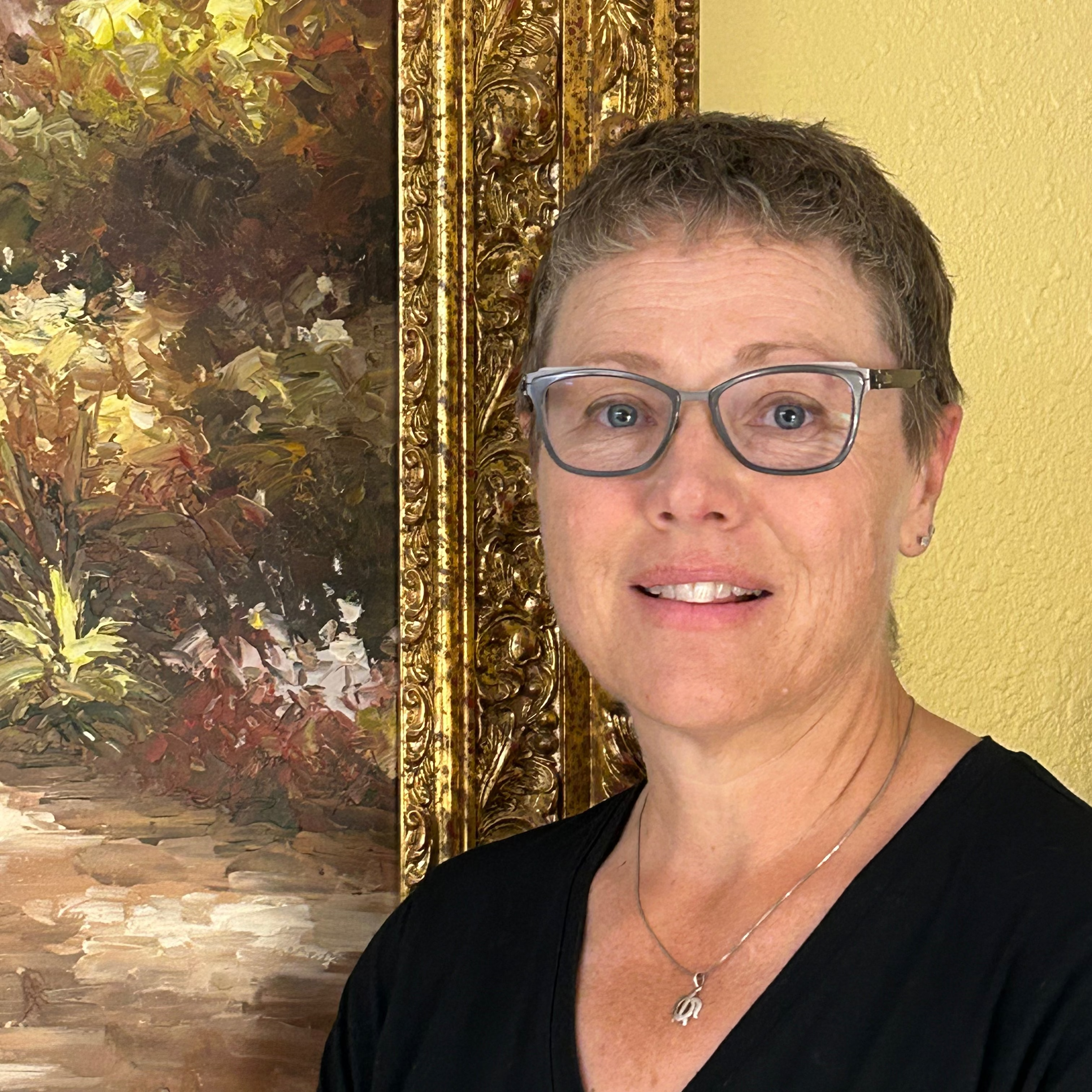 picture of woman with very short dark hair in front of painting