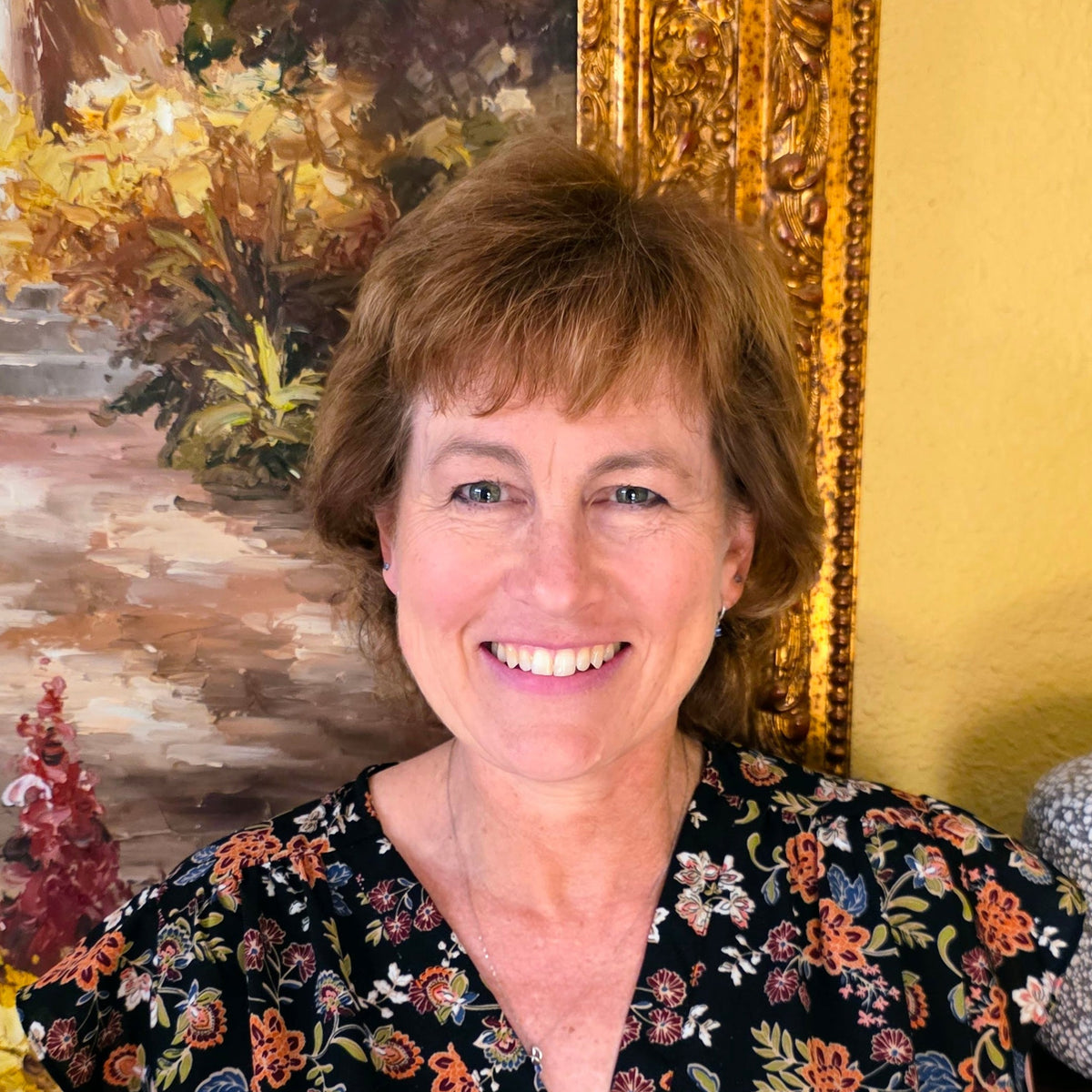 picture of woman with short reddish brown hair in front of painting